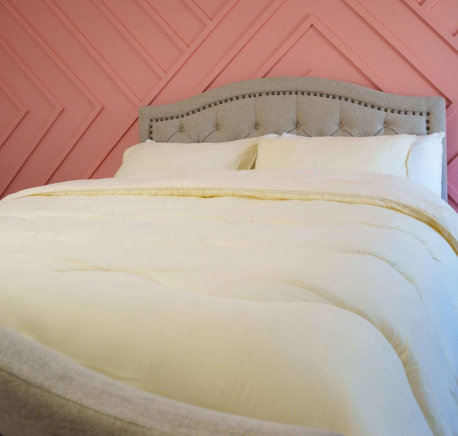 Cream white down comforter on bed with tufted headboard against pink geometric wall.