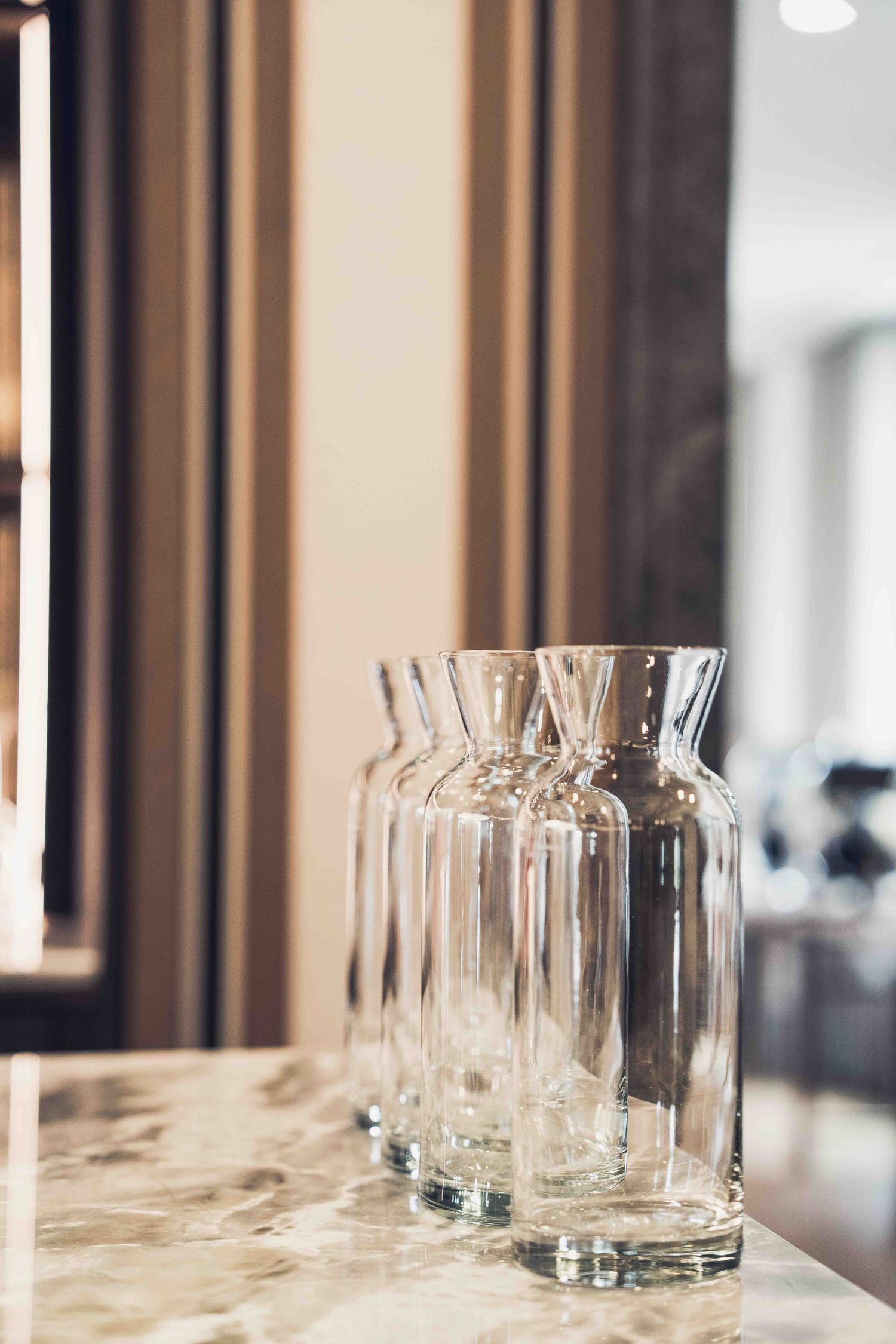 Row of empty glass water carafes lined up on a marble countertop in an elegant restaurant setting.