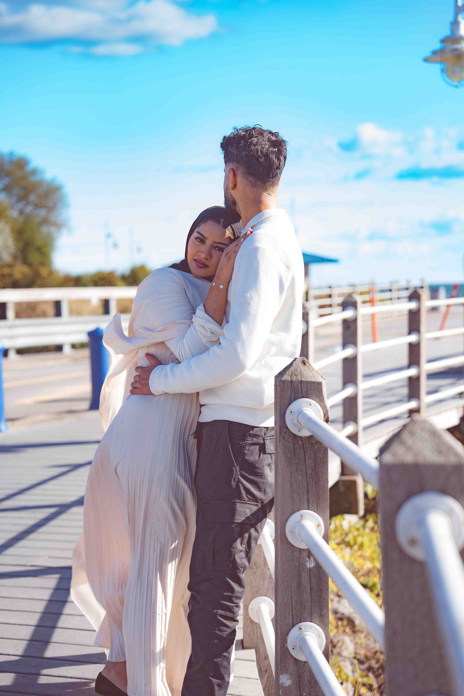 A tender moment shared between two people on a sunny boardwalk with white railings.