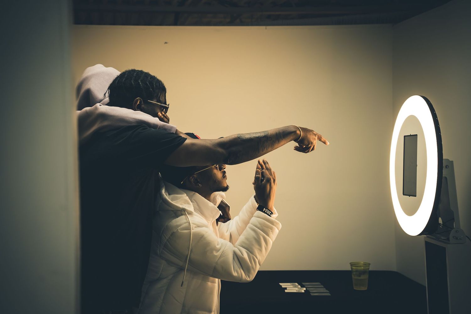 Person gesturing while standing next to a circular ring light in a room.