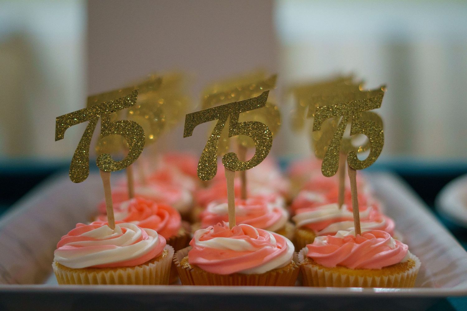 Row of pink cupcakes decorated with gold number 75 toppers for birthday celebration.