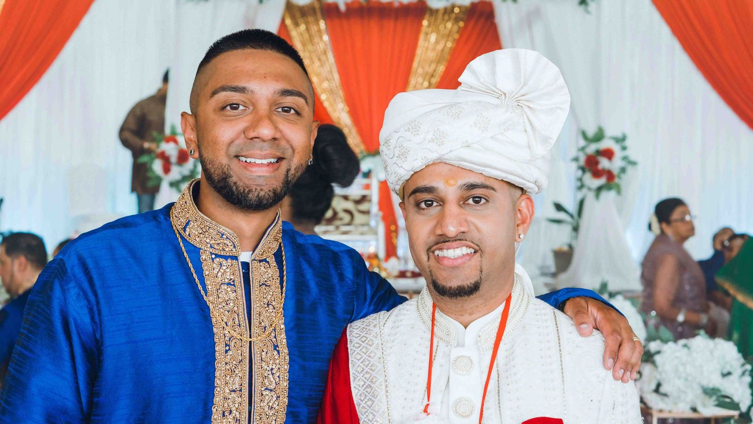Two guests at an Indian wedding wearing traditional formal attire pose together.
