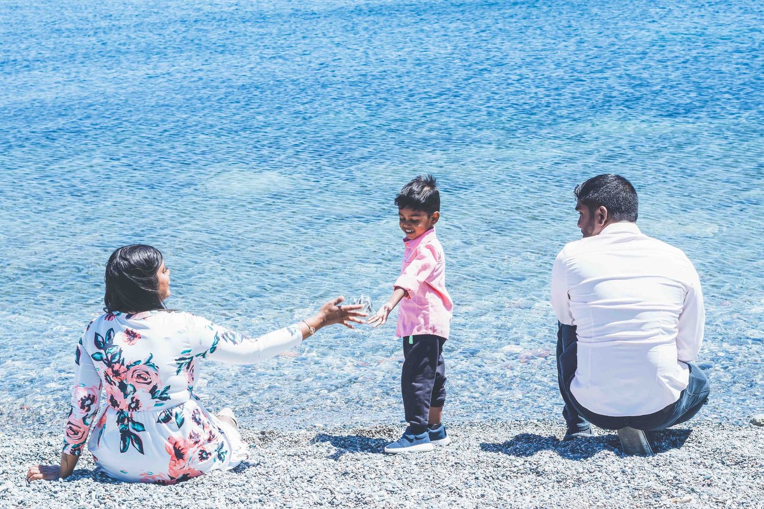 Group of people relaxing on a rocky beach shoreline overlooking calm blue waters.