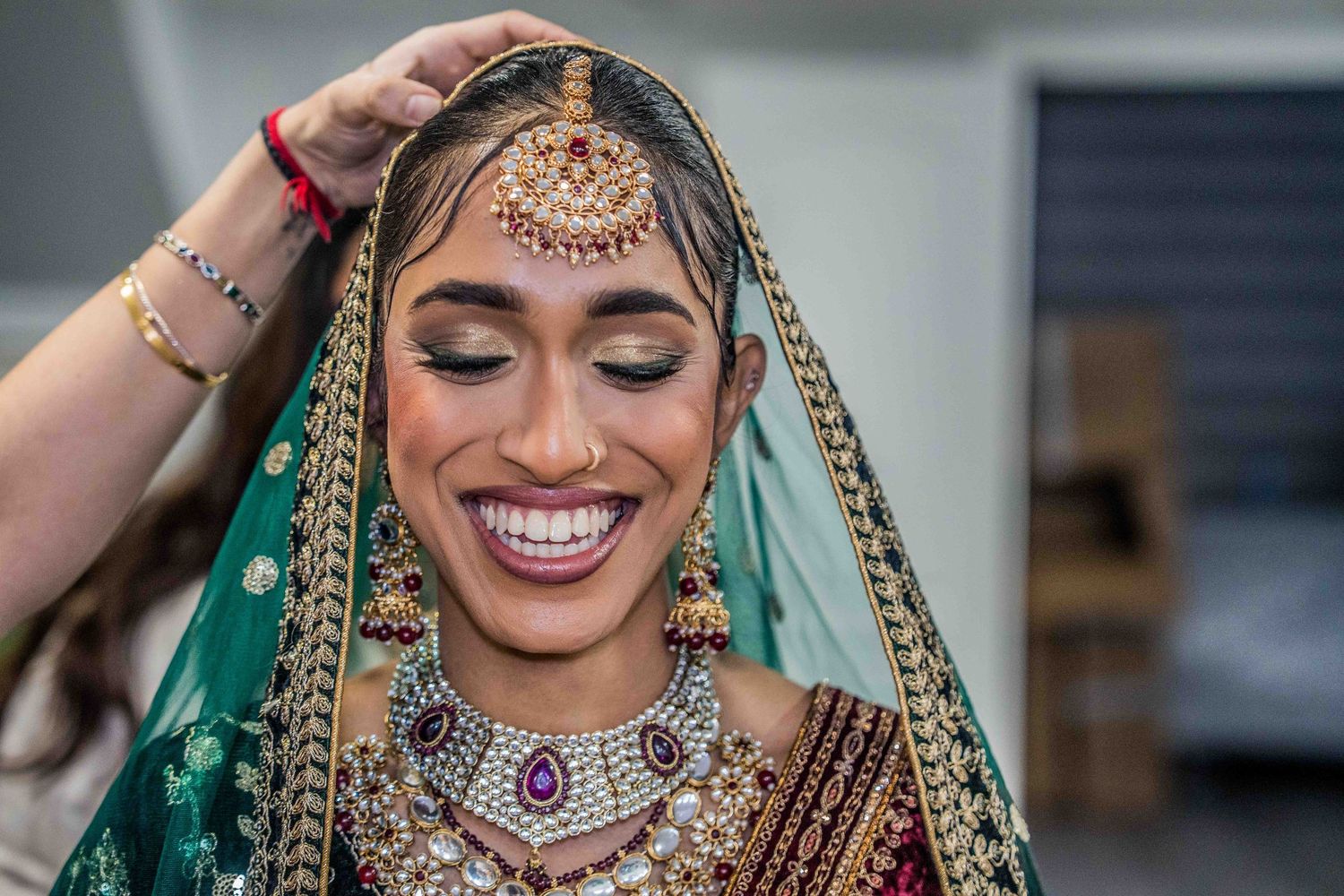 Traditional Indian bride wearing an ornate red and green lehenga with detailed gold embroidery and jewelry.