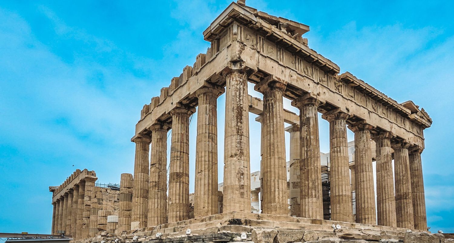 Panoramic view of the Parthenon temple ruins on Acropolis hill against bright blue sky.