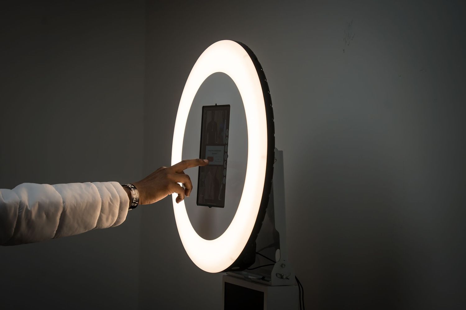 Arm reaching to touch an interactive display mounted in a circular light ring.