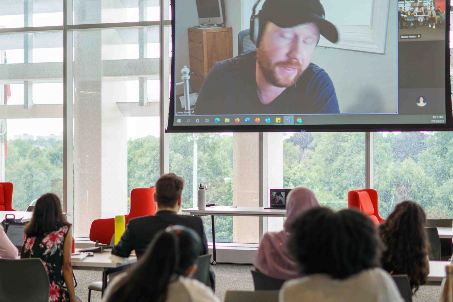 Modern classroom interior with desks and chairs arranged in rows facing digital displays.