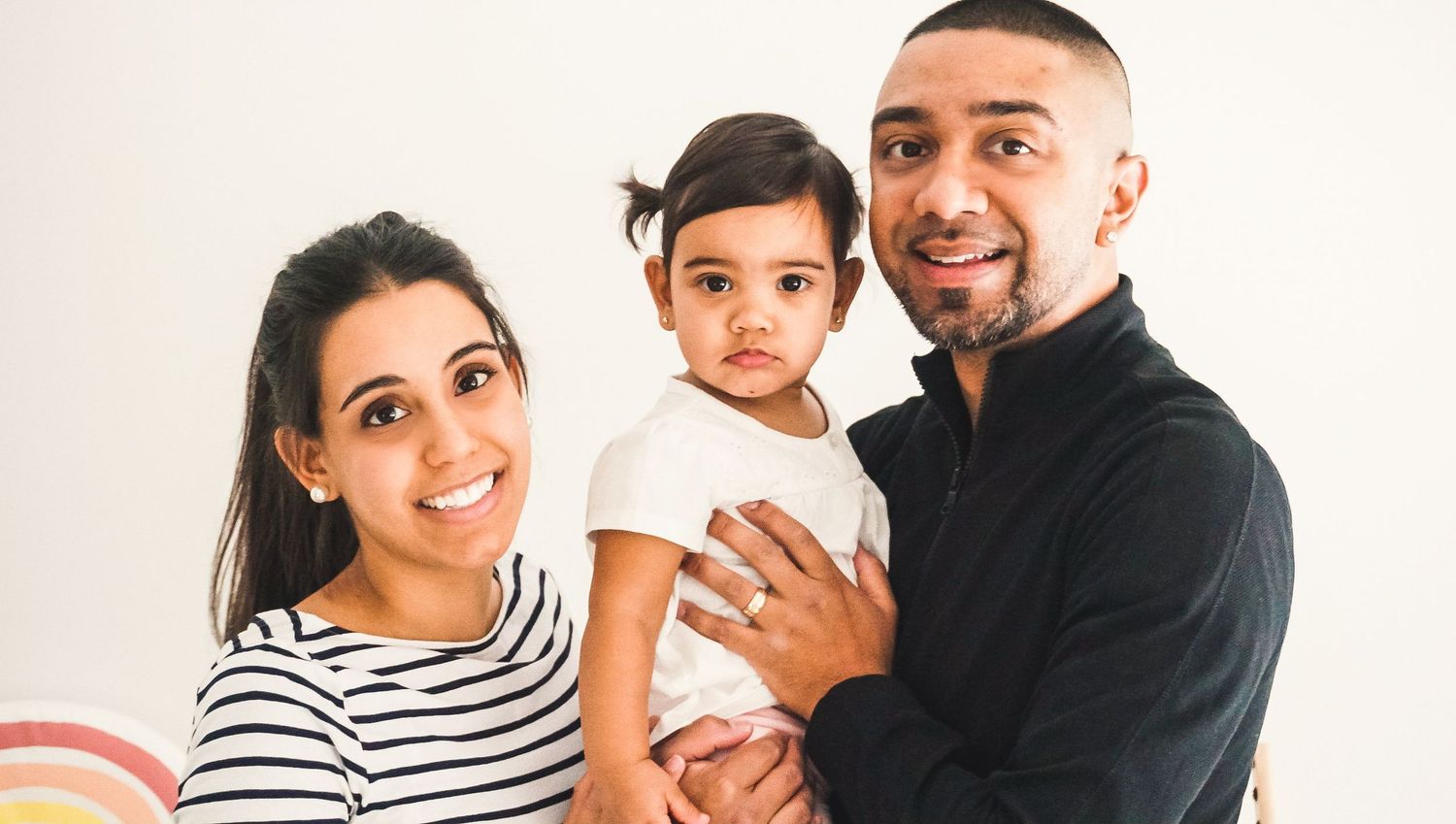 Studio family photoshoot with parents and child against white background.