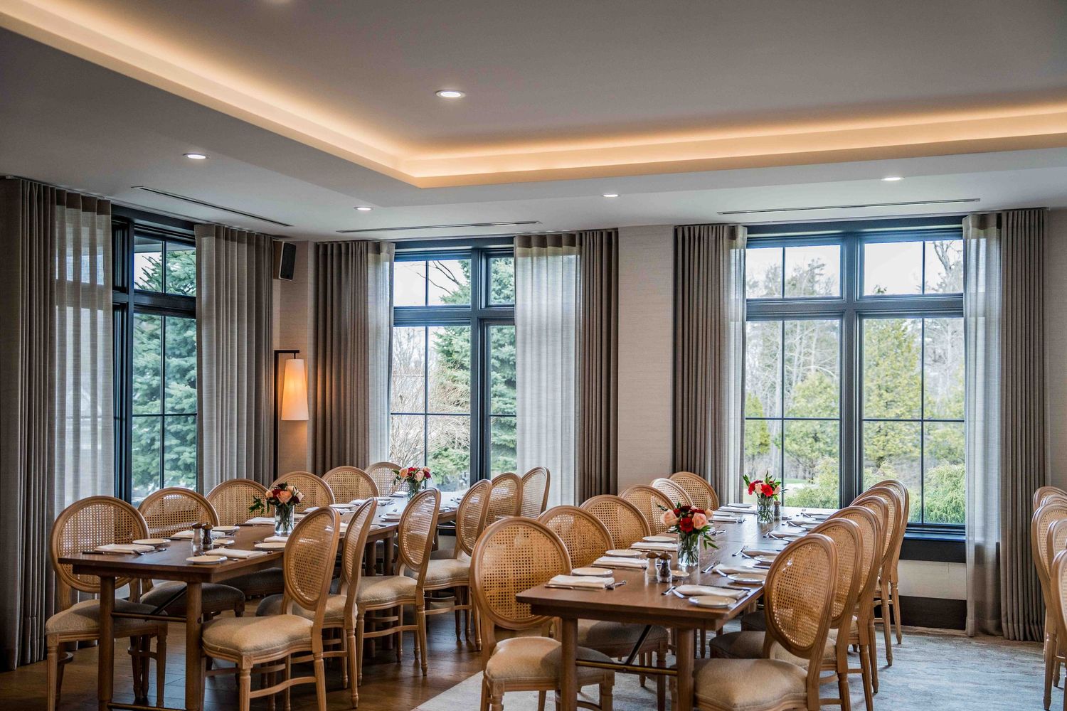 Elegant private dining room with large windows, wooden tables, and upholstered chairs set for a formal meal.