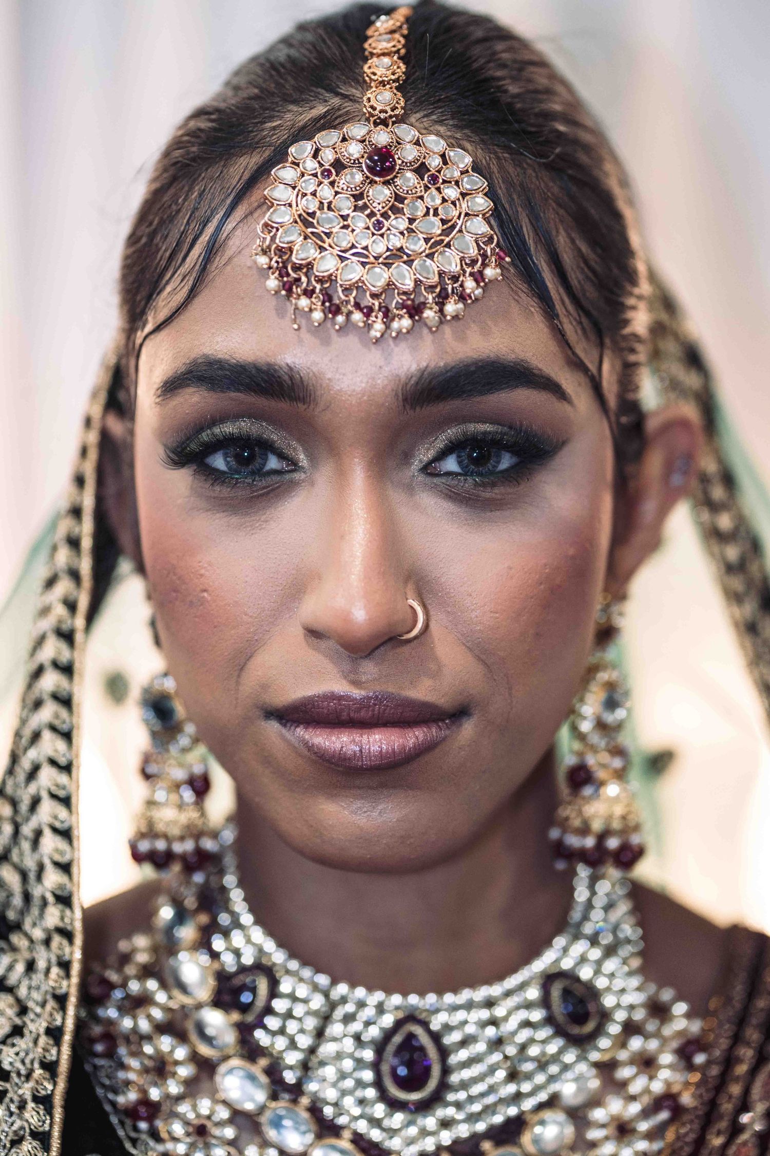 Traditional Indian bridal jewelry featuring an ornate tikka headpiece, statement necklace and earrings with pearl and crystal details.