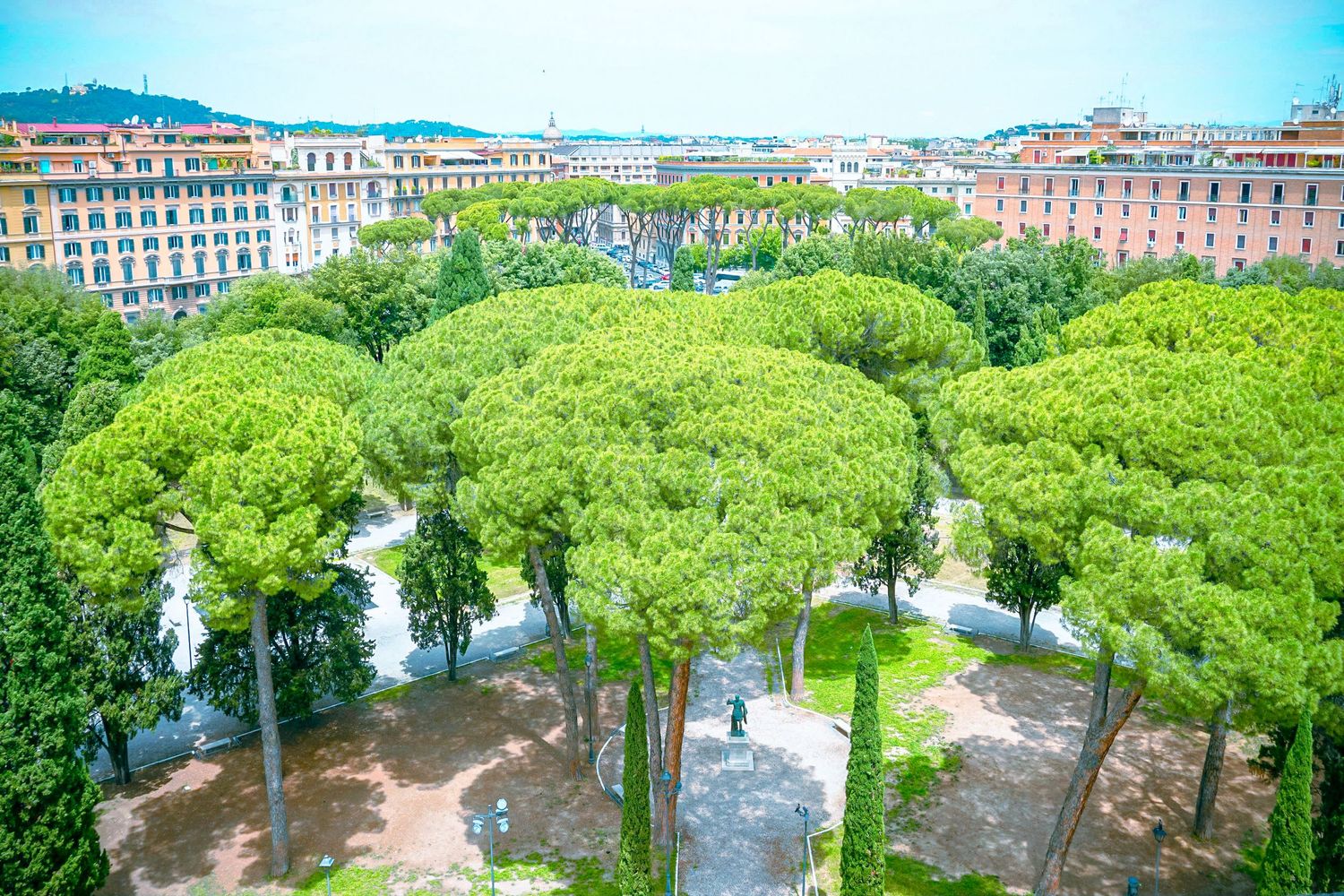 Aerial view of lush green park with stone pathways surrounded by urban buildings.