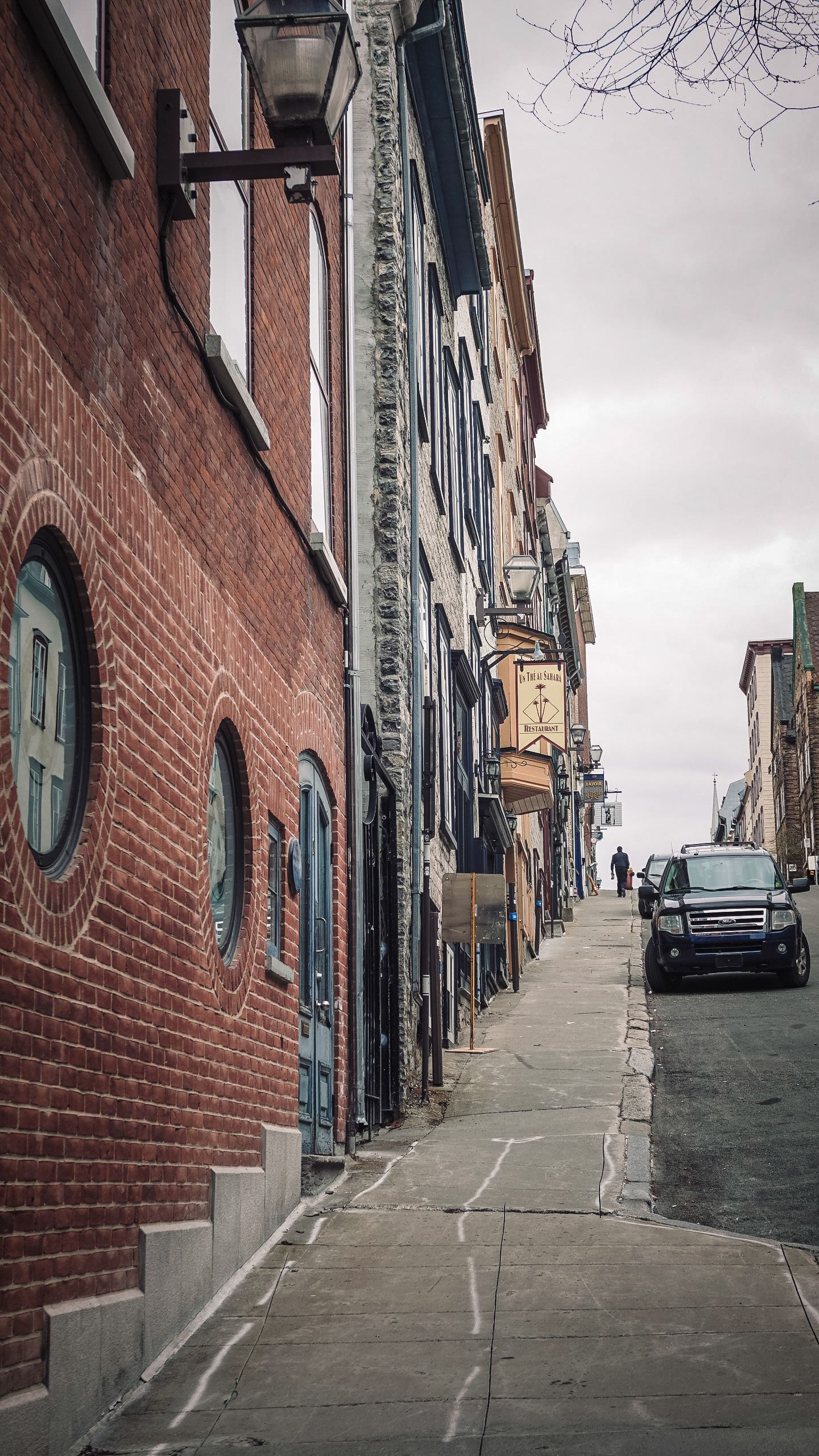 Steep brick-lined street with historic buildings and parked cars in an old city quarter.