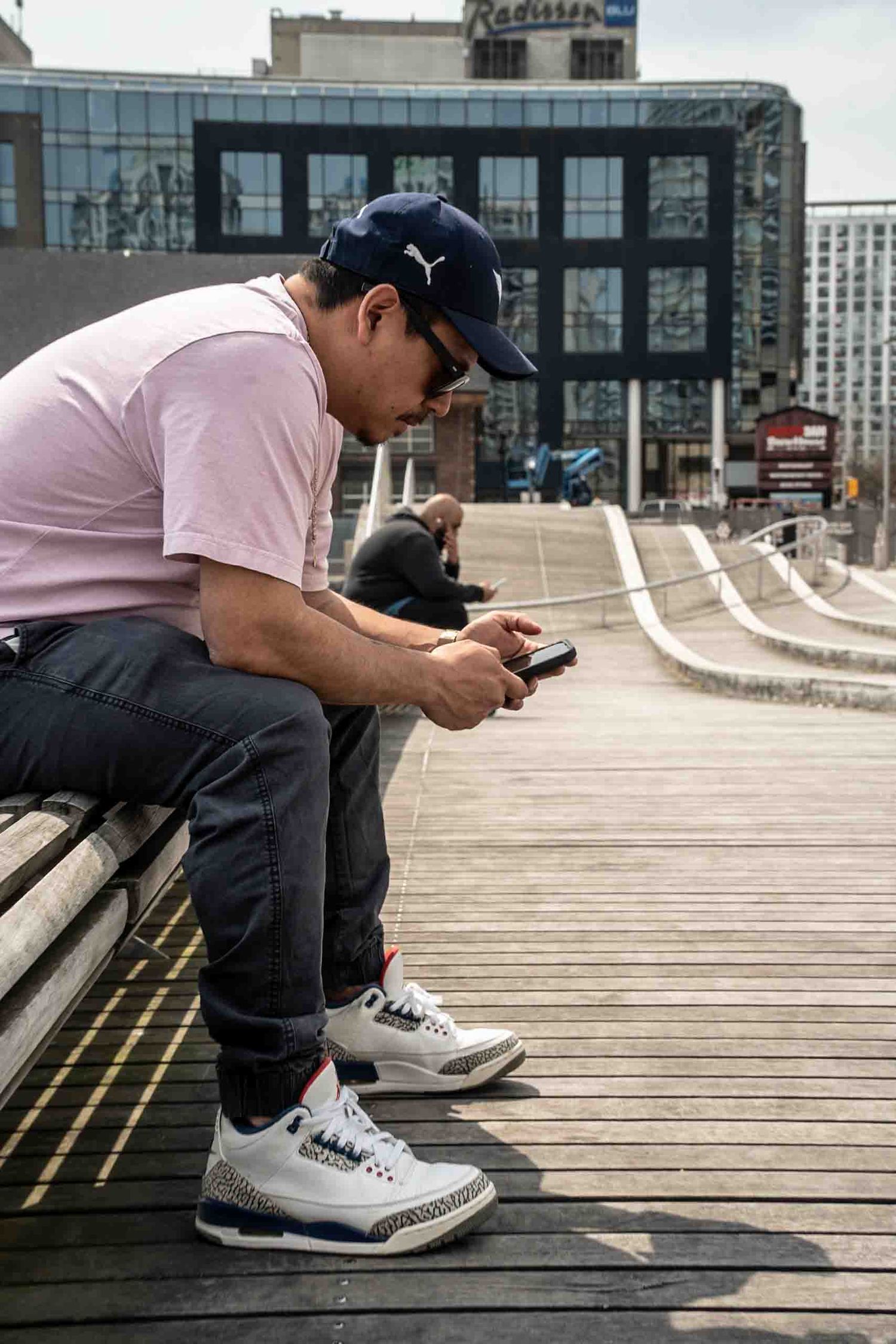 Person in casual attire sitting on wooden deck with urban buildings in background.