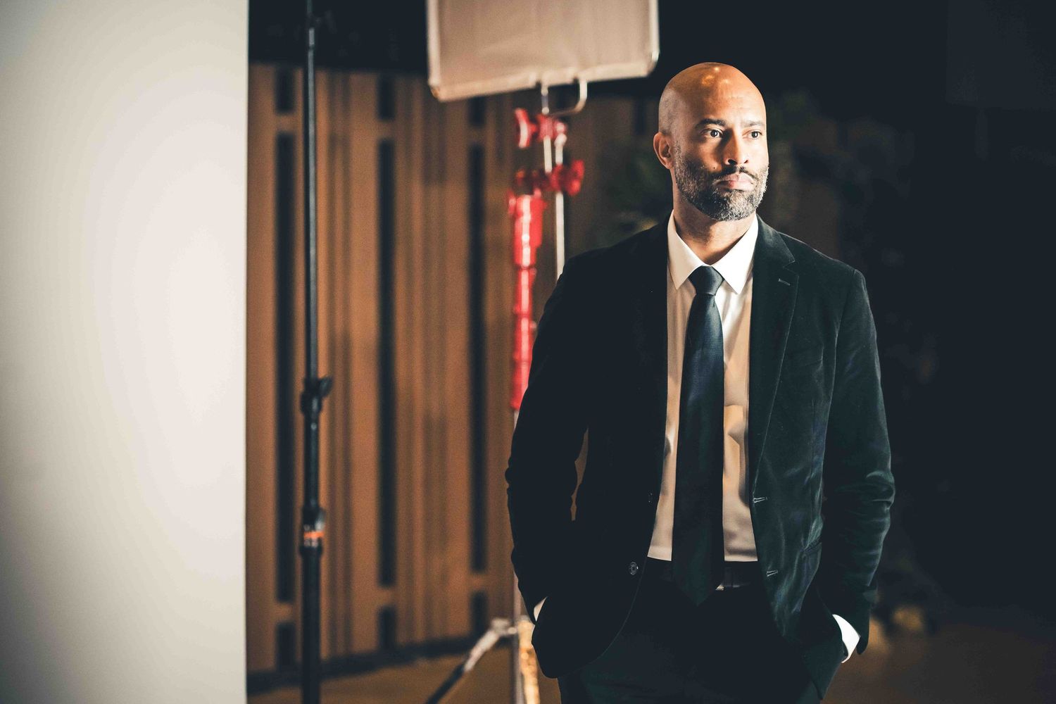 A groom in a dark suit and tie poses against a moody, dramatic background.
