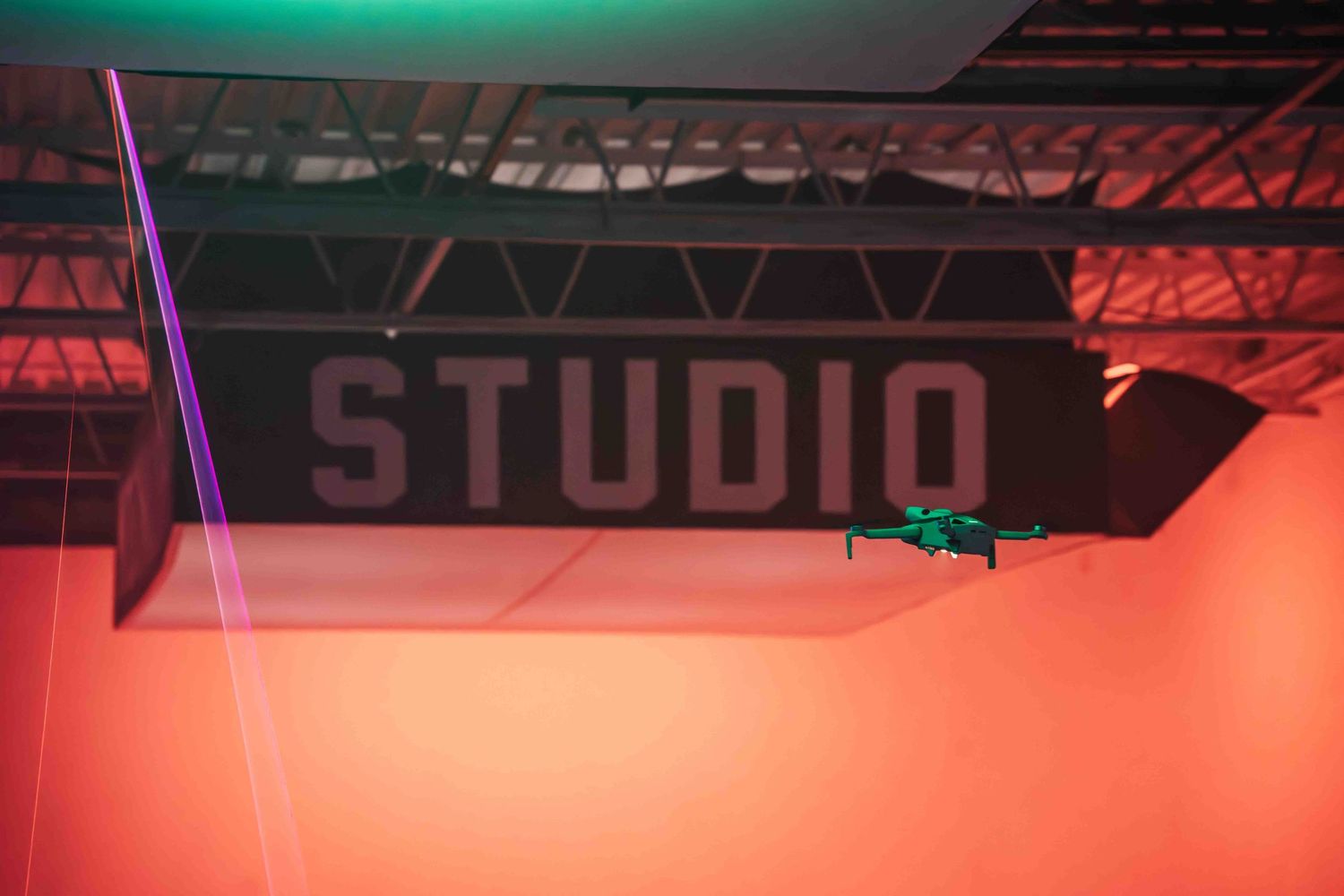 A small drone hovers in a studio space illuminated by red and green lighting.