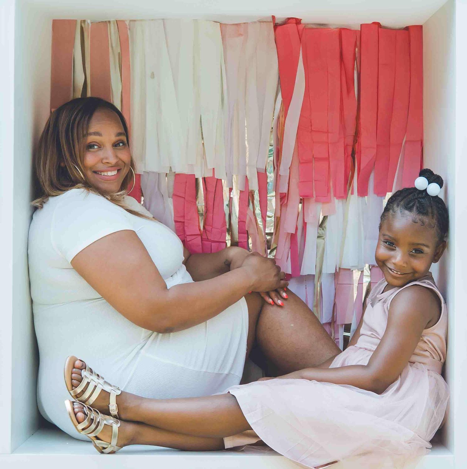 People lounging in casual attire against a backdrop with pink and white streamers.