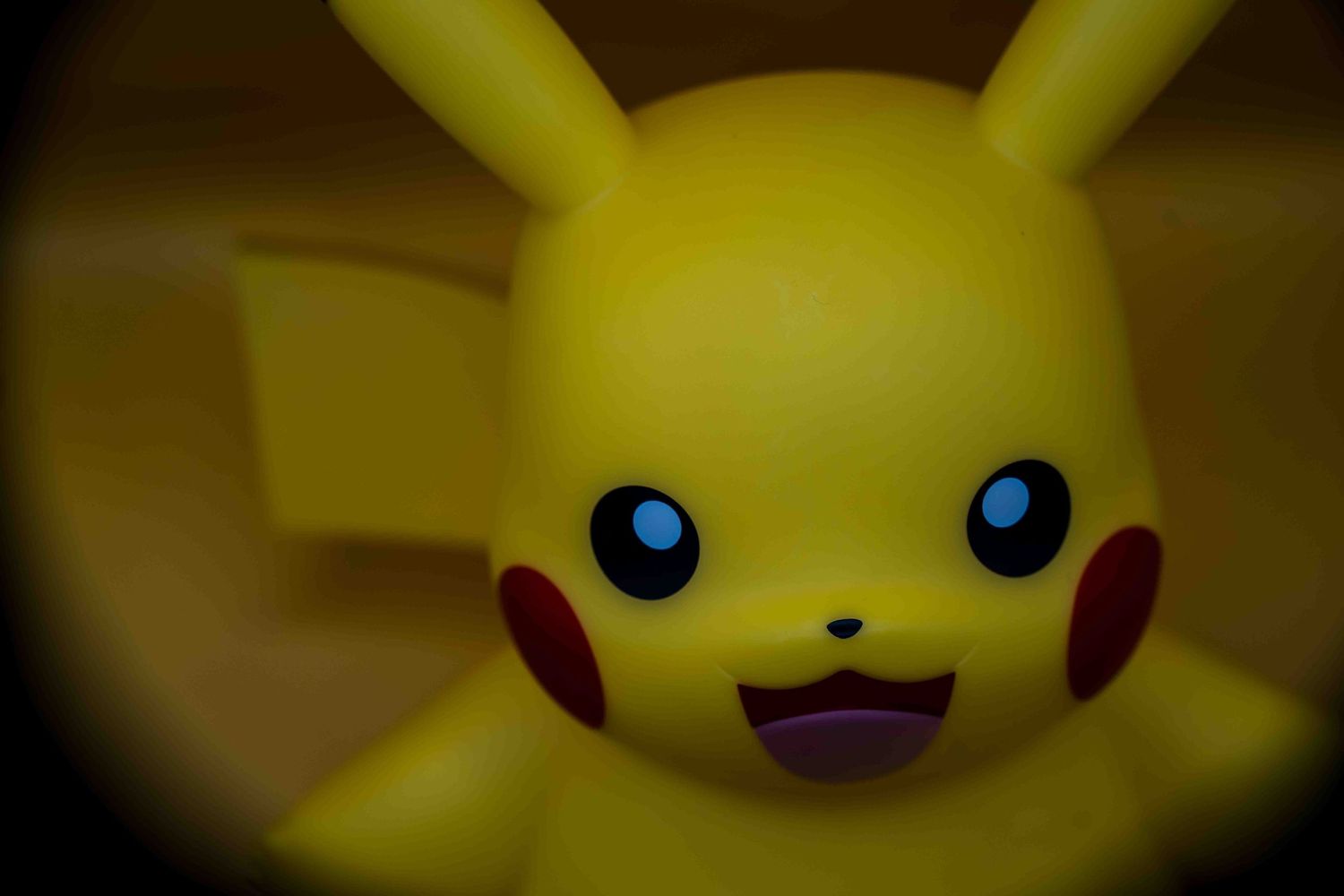 Close-up of a yellow Pikachu Pokemon figurine with blue eyes and red cheeks against a dark background.