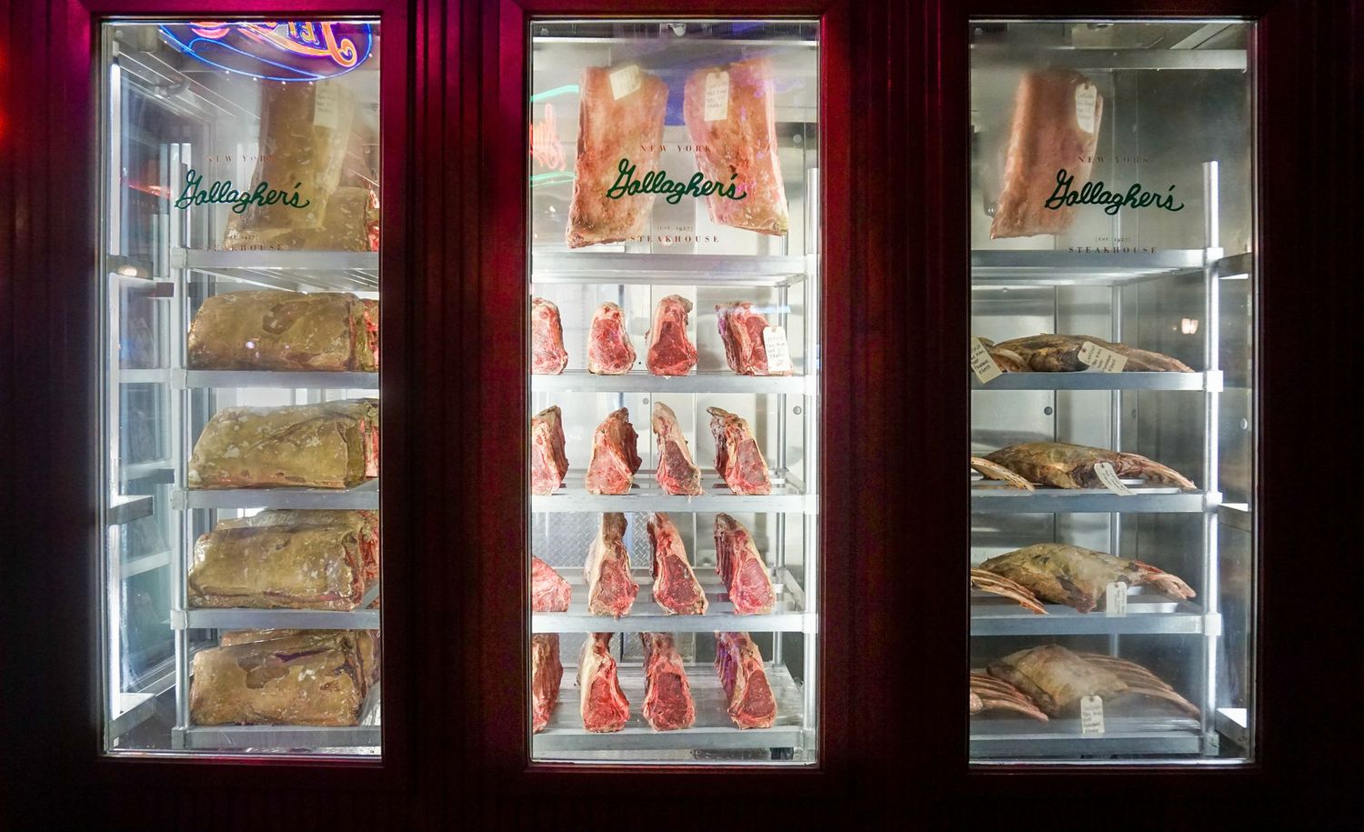 Illuminated meat display case showing hanging cuts of meat and stored products on shelves.