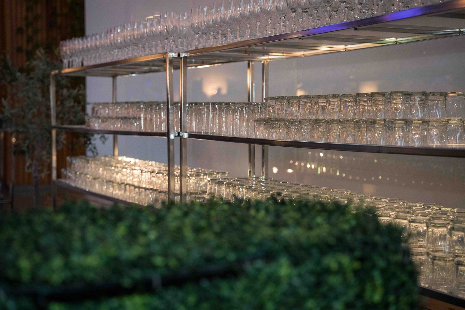 Long display of wine glasses arranged on shelves with ambient lighting in an upscale restaurant.