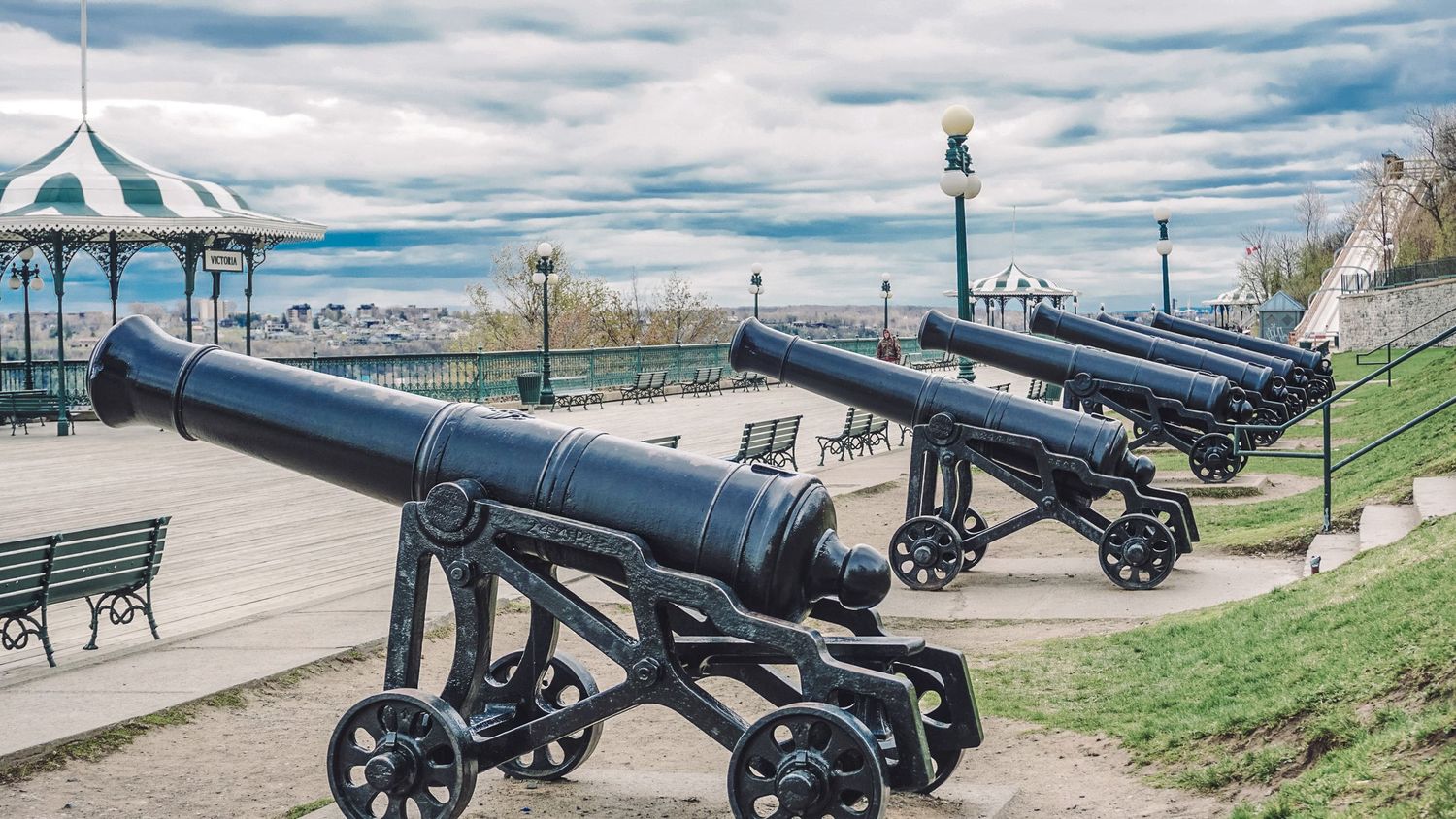 Row of historic cannons displayed along a waterfront promenade.