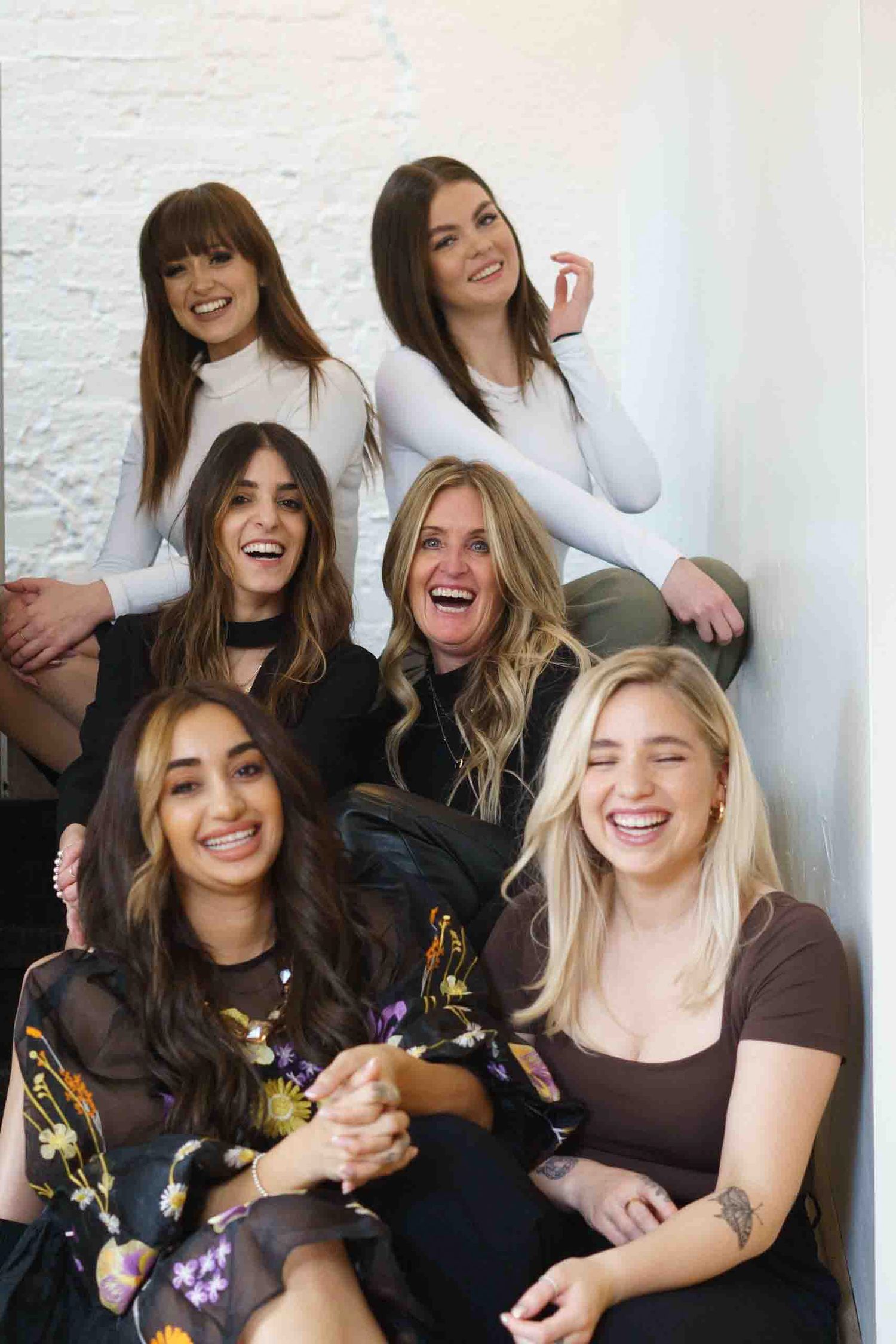 Group photo of salon team members smiling together against white wall.