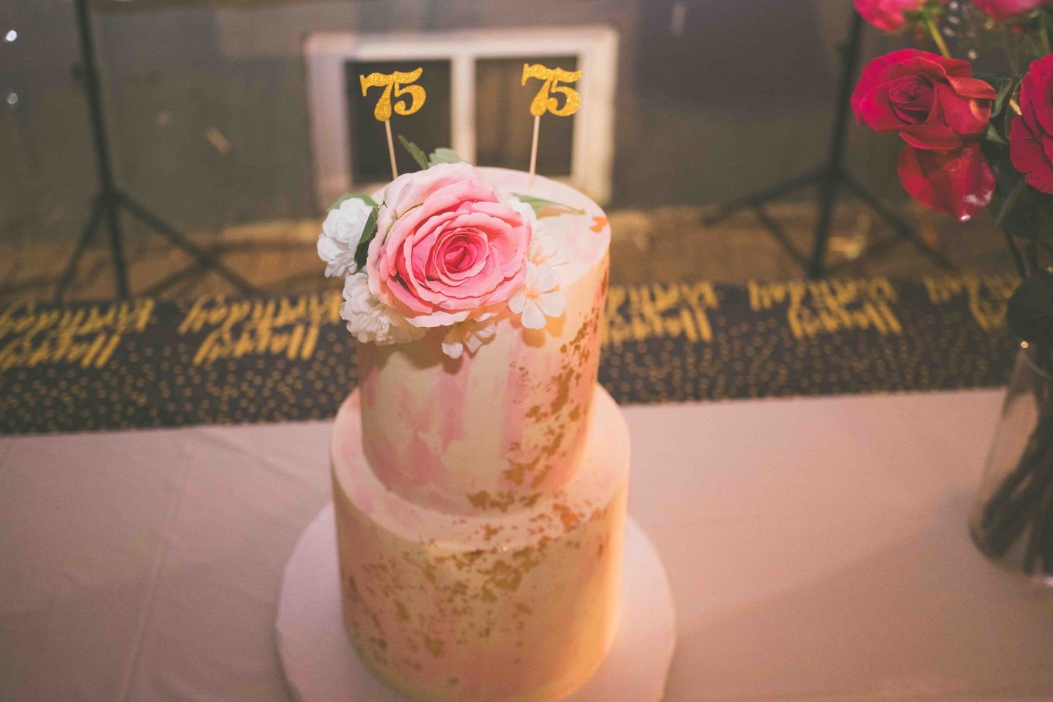 Side view of an elegant two-tiered birthday cake with pink and gold accents.