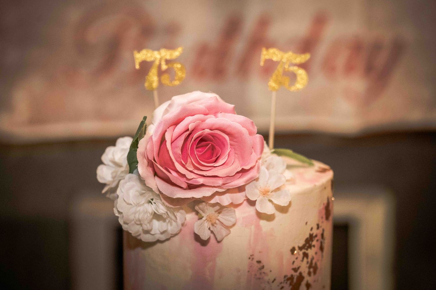 Close view of a pink and white celebration cake with gold number toppers.