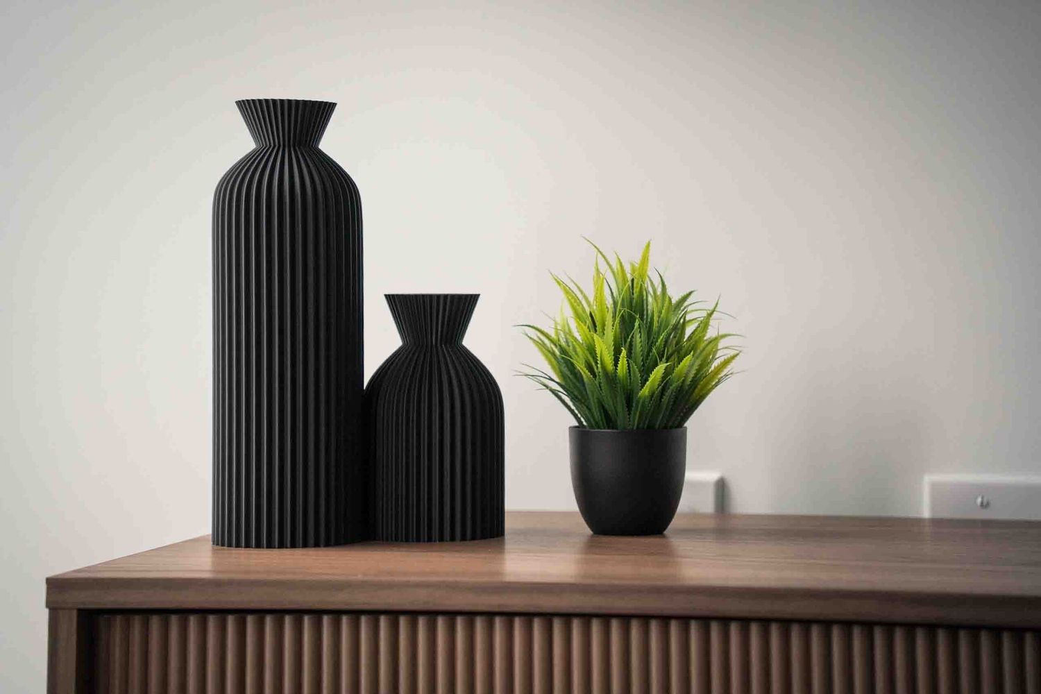 Minimalist home decor display with black vases and plants on wooden surface.