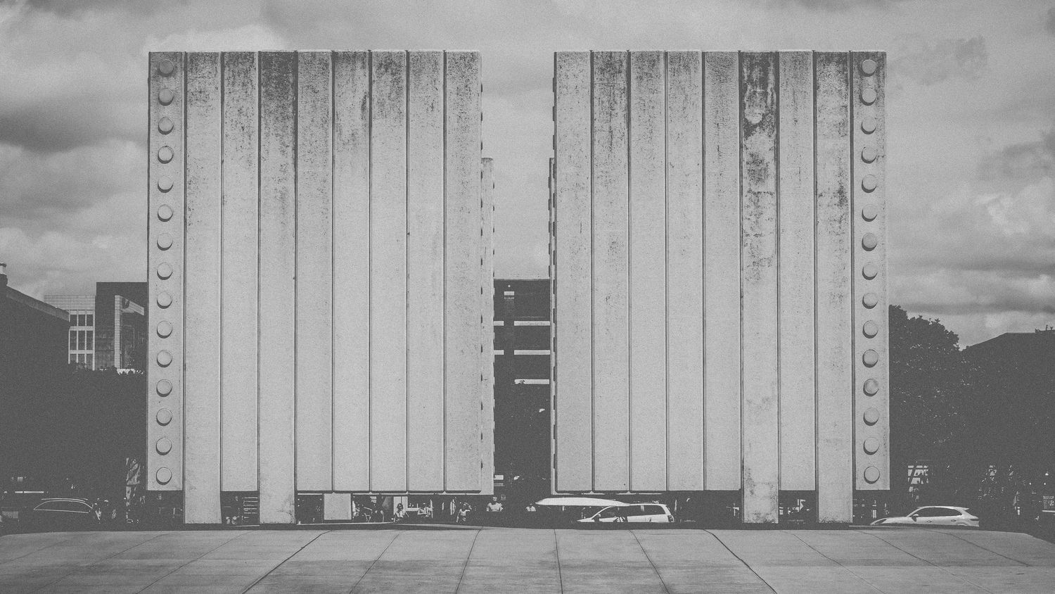 Minimalist black and white photograph of two tall modernist buildings with vertical striped patterns.