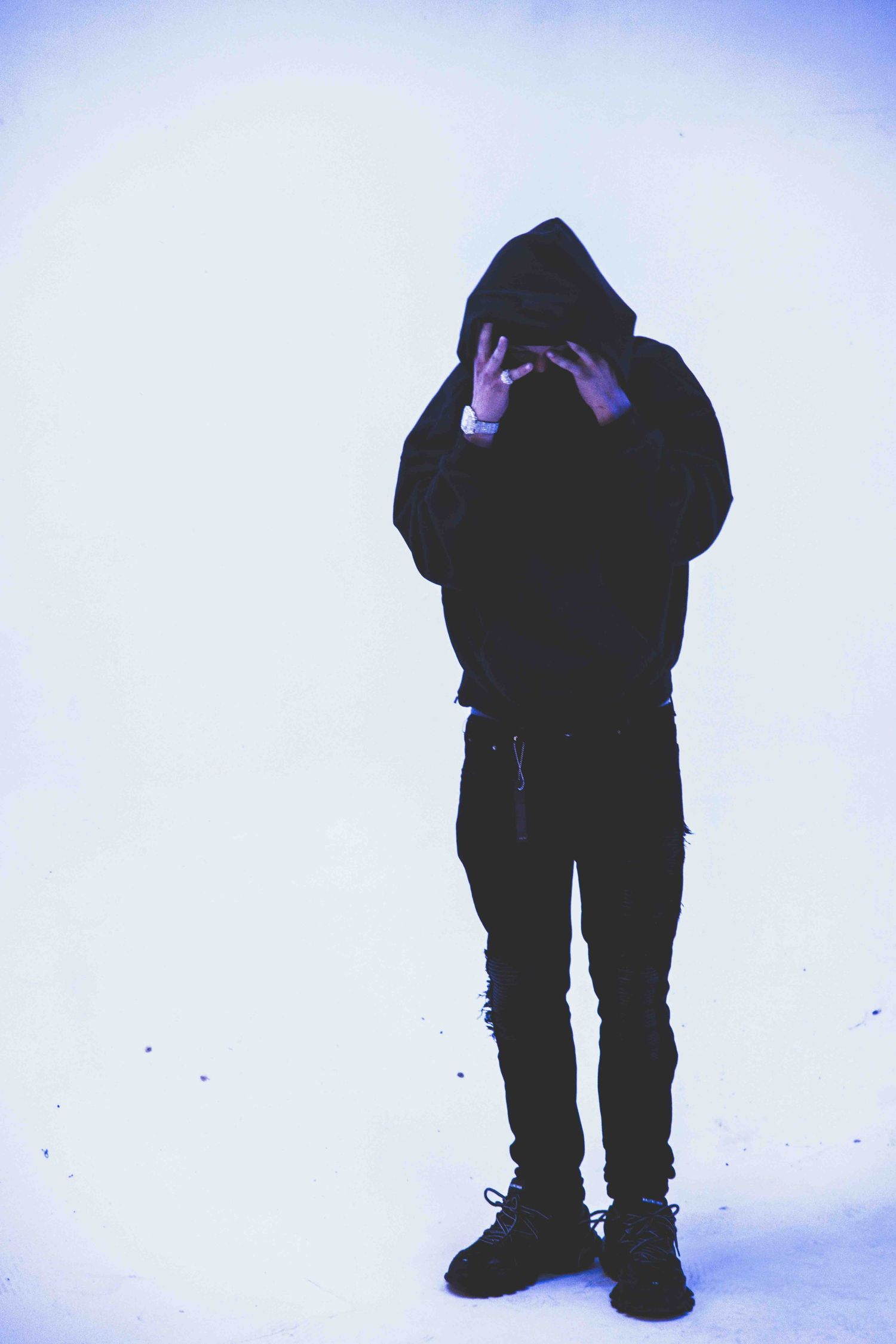 Silhouette of person in black hoodie and pants making hand gestures against light background.