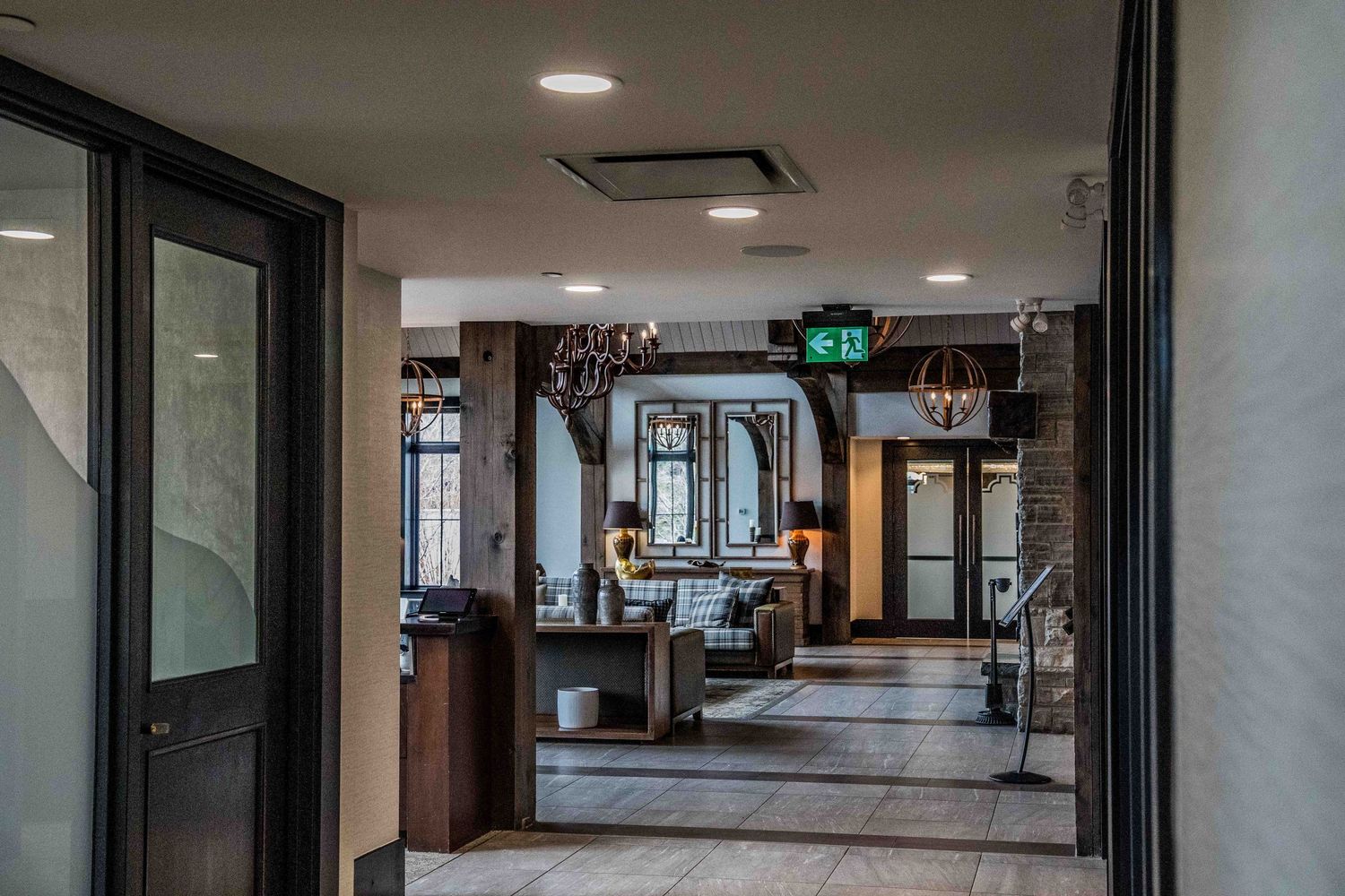 Elegant hotel lobby corridor with dark wood accents, chandelier lighting, and modern reception area visible in background.