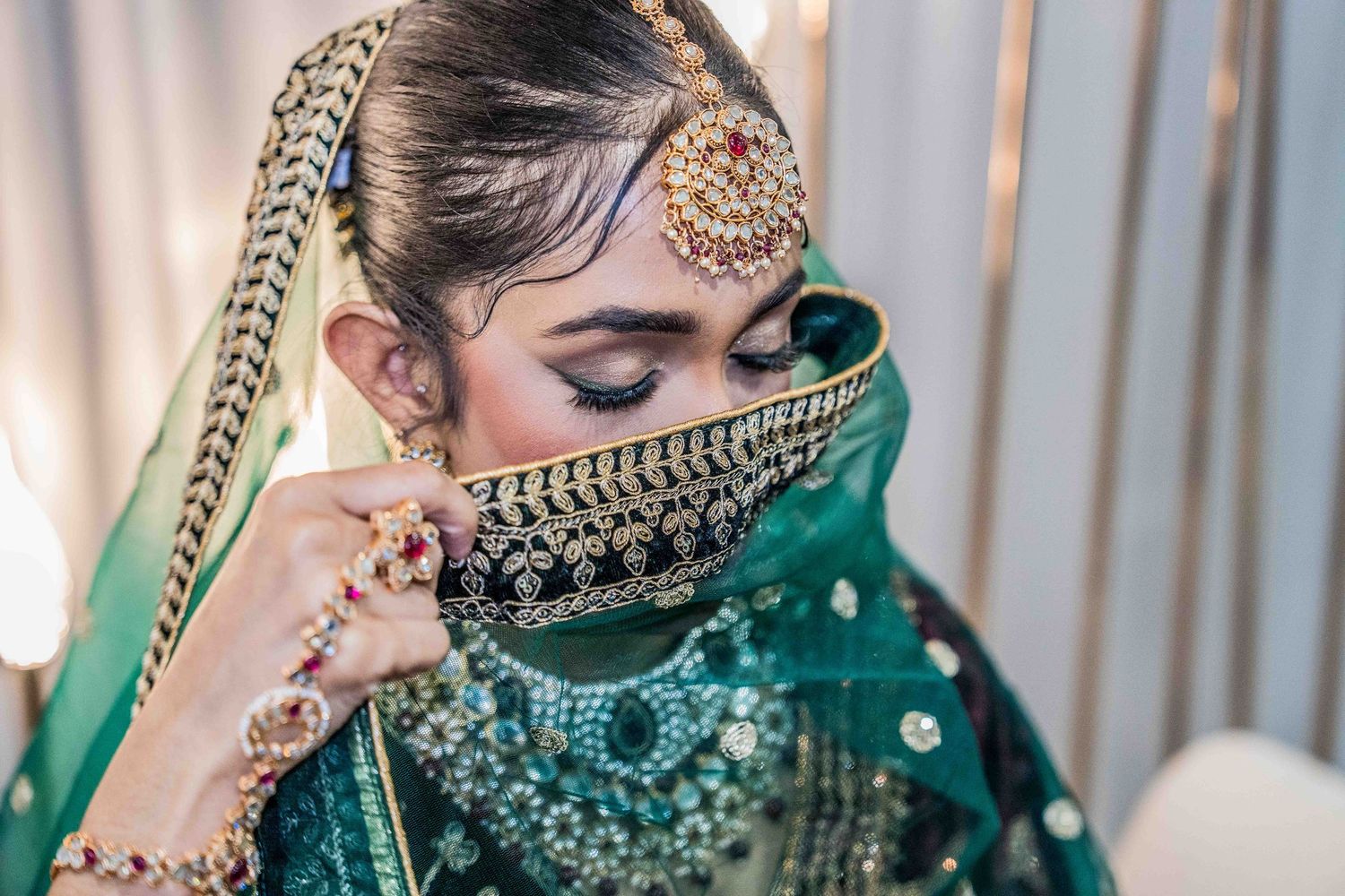 A bride in an emerald green lehenga with gold jewelry and traditional Indian bridal attire poses for photos.