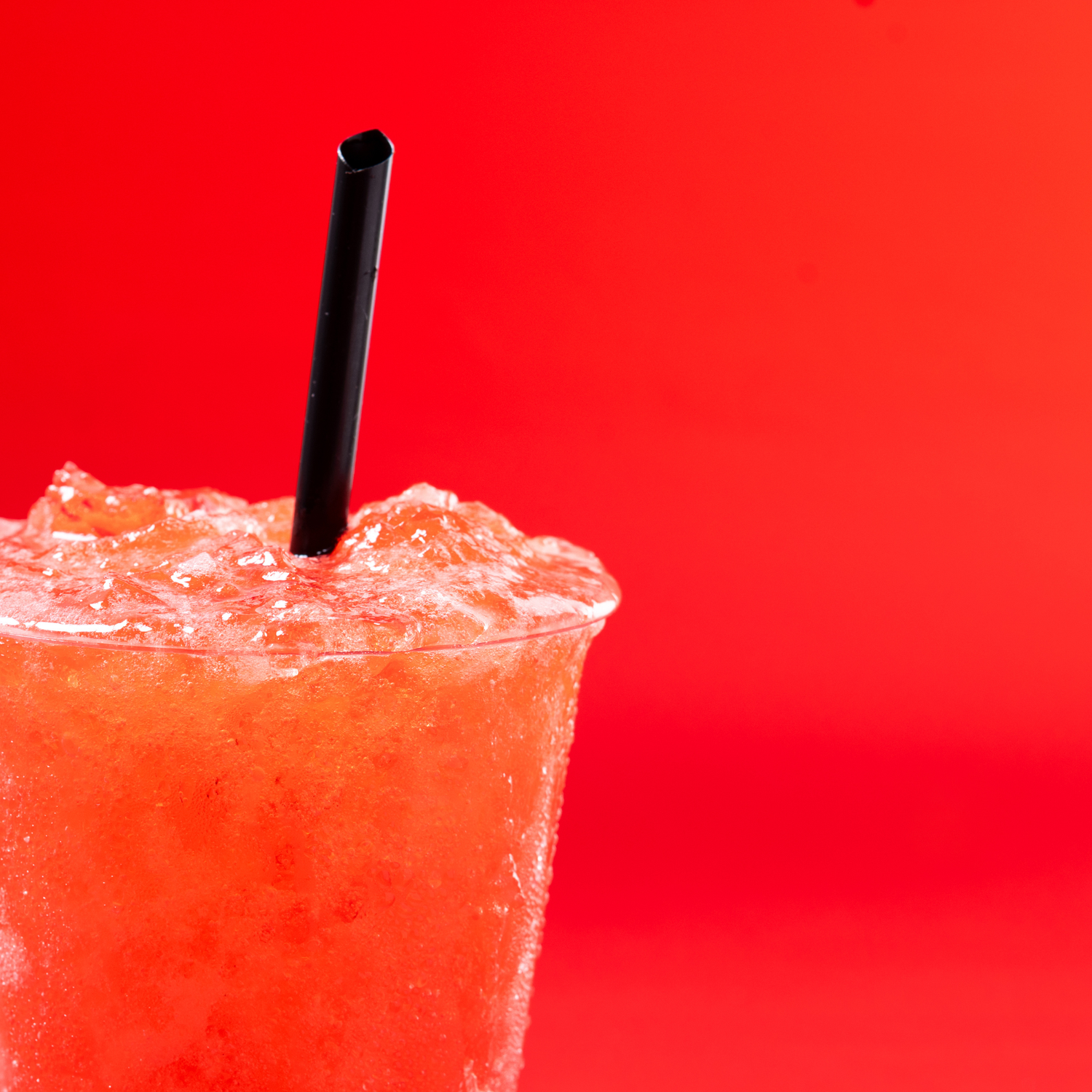 Three frosty pink frozen cocktails with black straws on a bright red background.