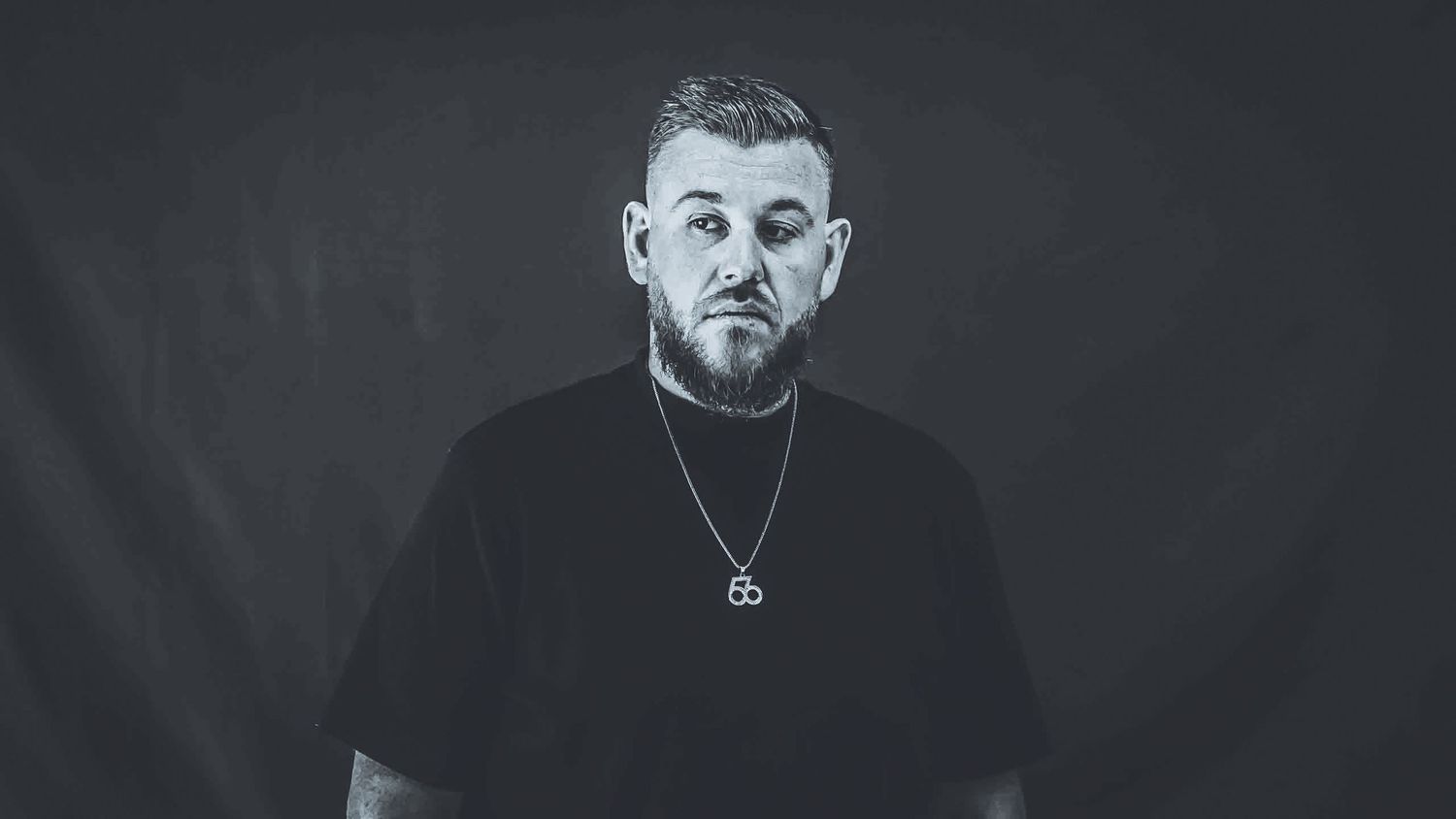 Studio portrait of person in black t-shirt against dark background with dramatic lighting.