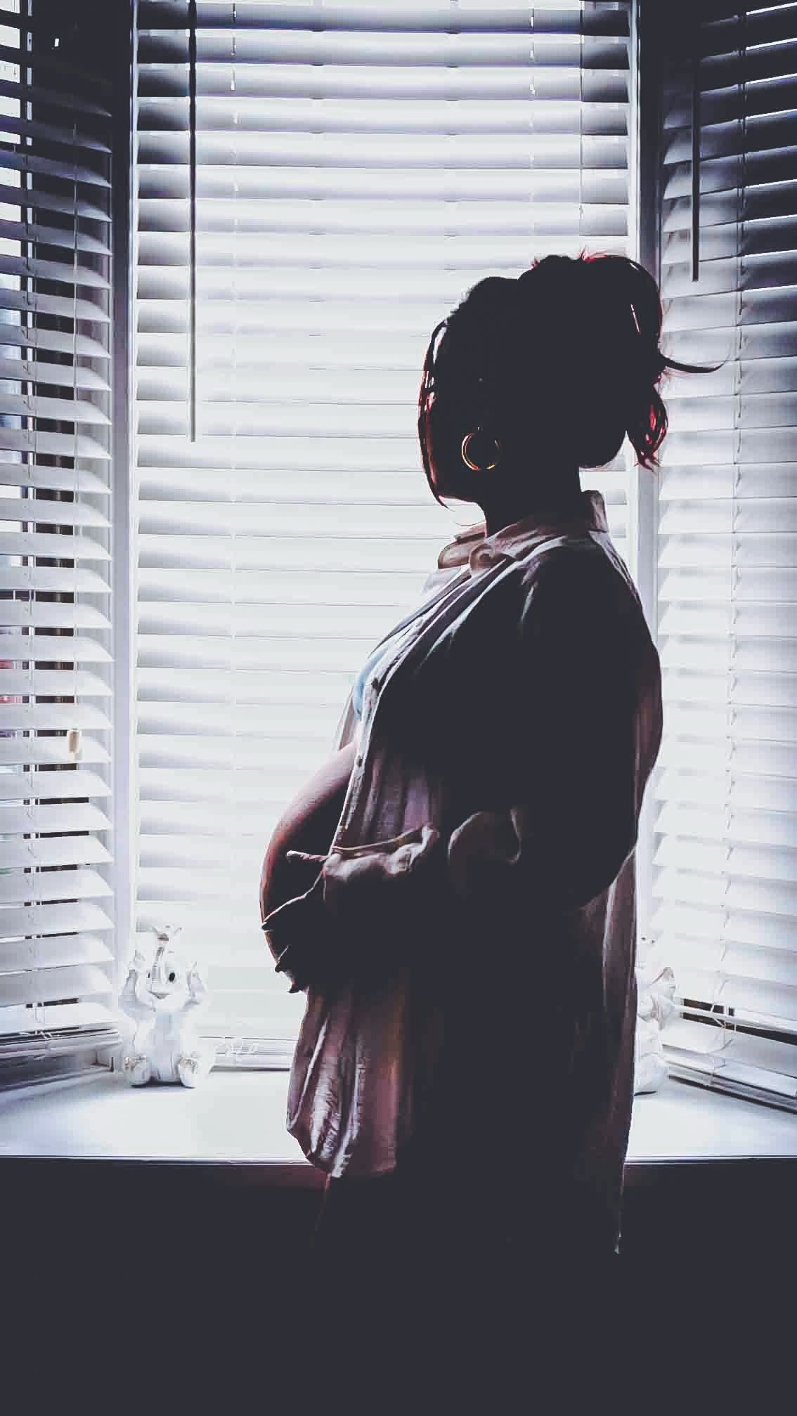 Silhouette figure standing by window with venetian blinds casting dramatic shadows.
