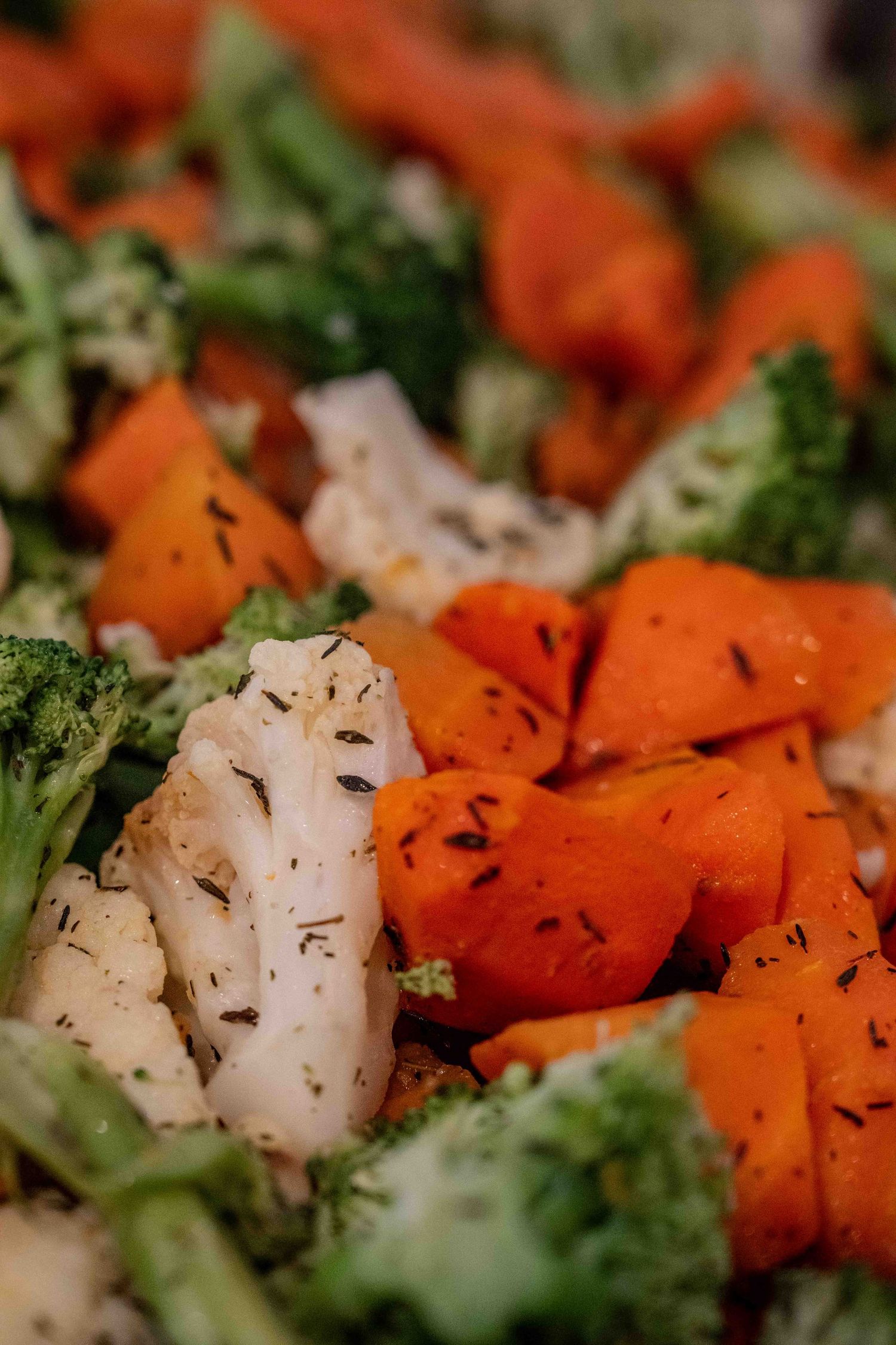 Colorful roasted vegetables including carrots, broccoli, and cauliflower seasoned with herbs on a baking sheet.