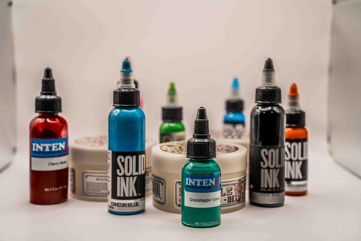 Assorted tattoo ink bottles including Solid Ink and Inten brands in various colors on a white background.
