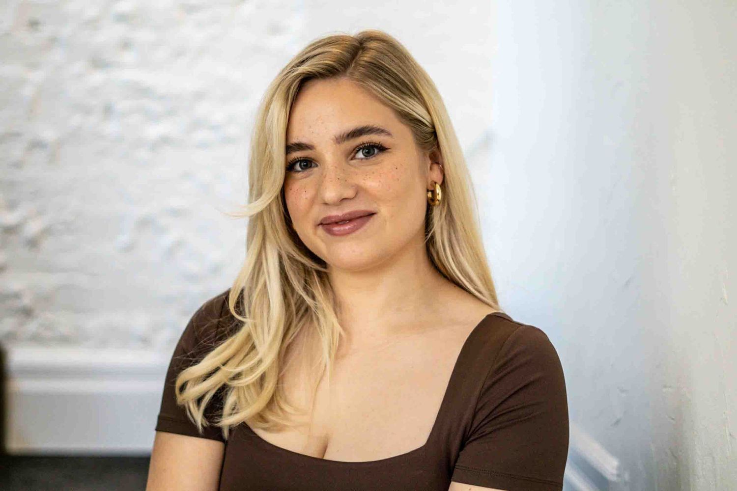 Professional salon portrait showcasing a brown square-neck top against white textured walls.