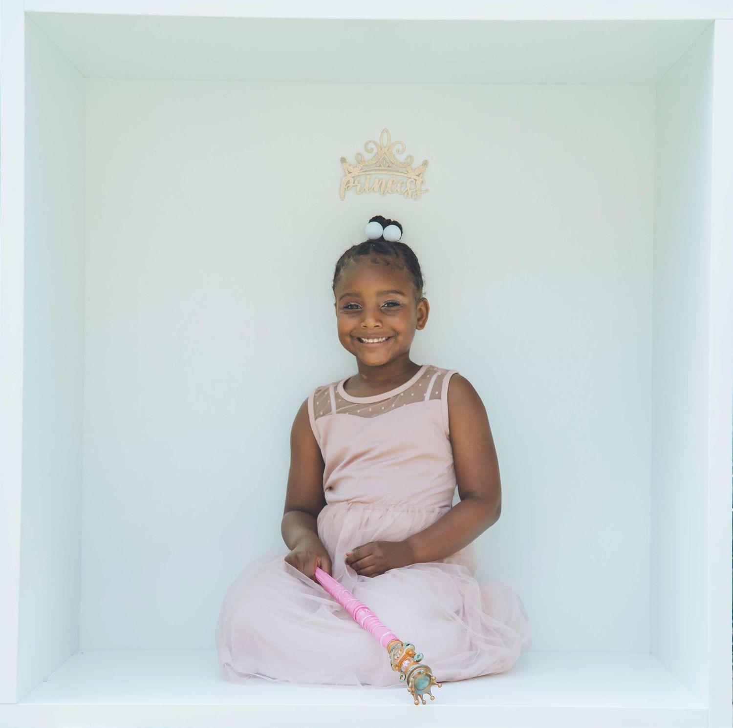 Person in a pink dress sitting in a white studio setting with decorative elements.