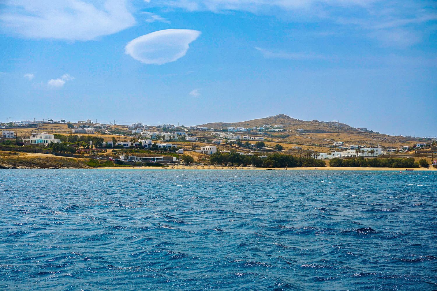 Coastal view of Greek island landscape with blue waters and distant mountains.