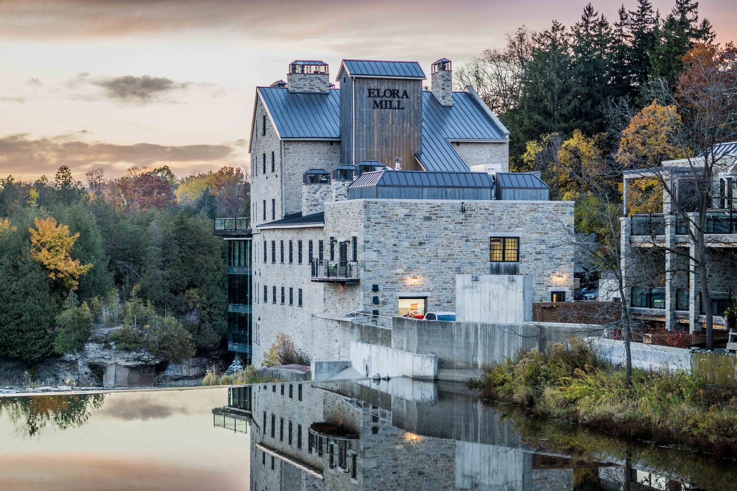 Historic stone flour mill building reflected in calm water at sunset.