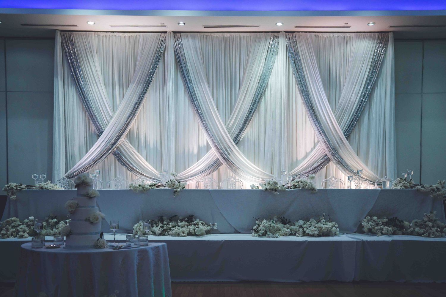 White draped fabric backdrop with blue uplighting for an elegant event setting.