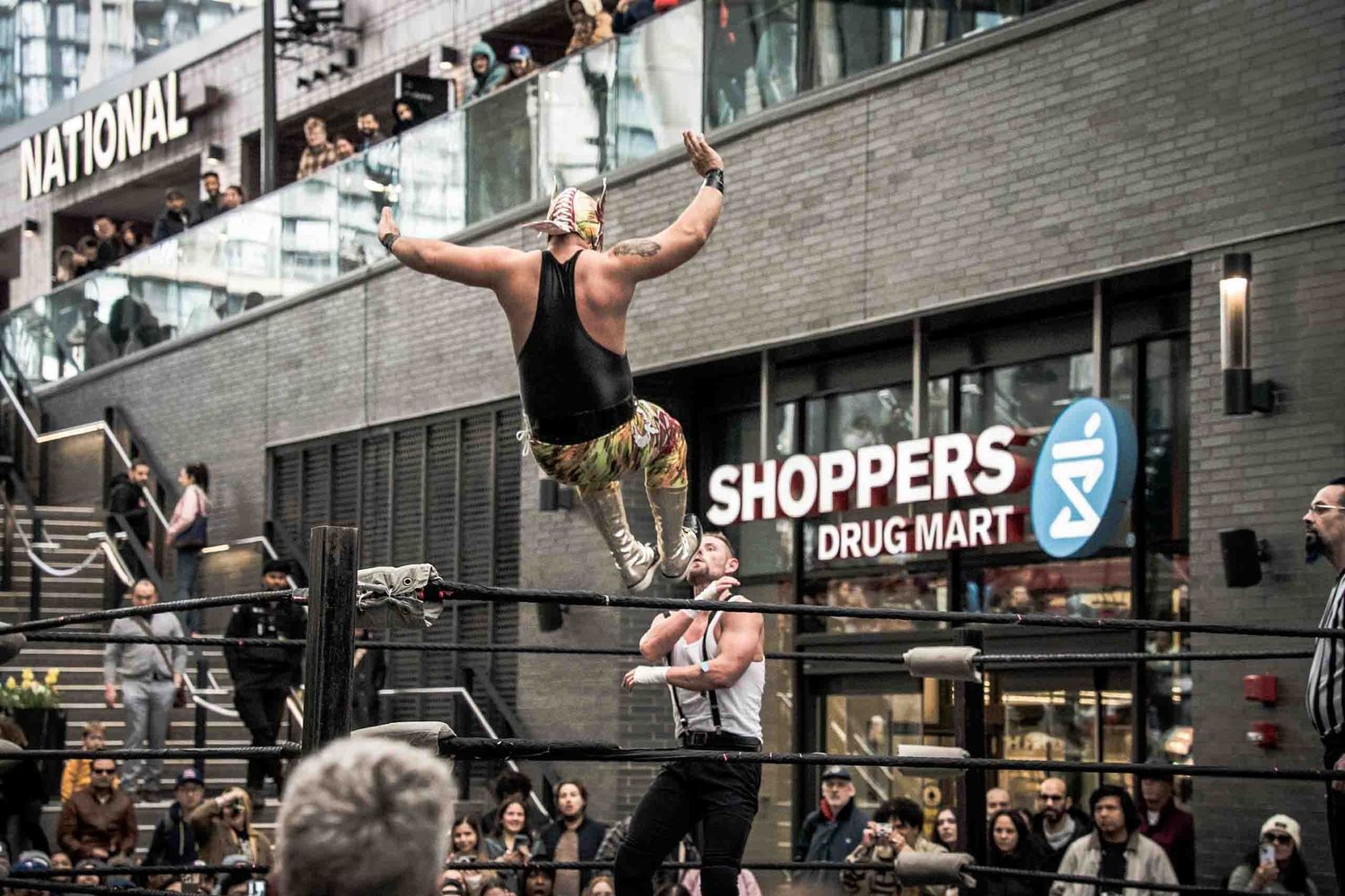 Urban street scene with people jumping in front of retail storefronts.