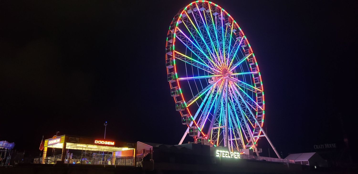 Illuminated ferris wheel glowing with colorful lights against night sky.