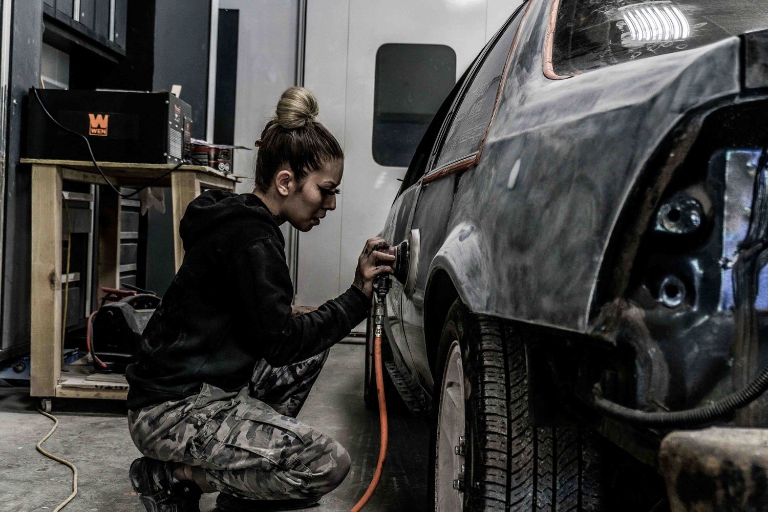 Someone in dark clothing working on detailing a car's exterior.