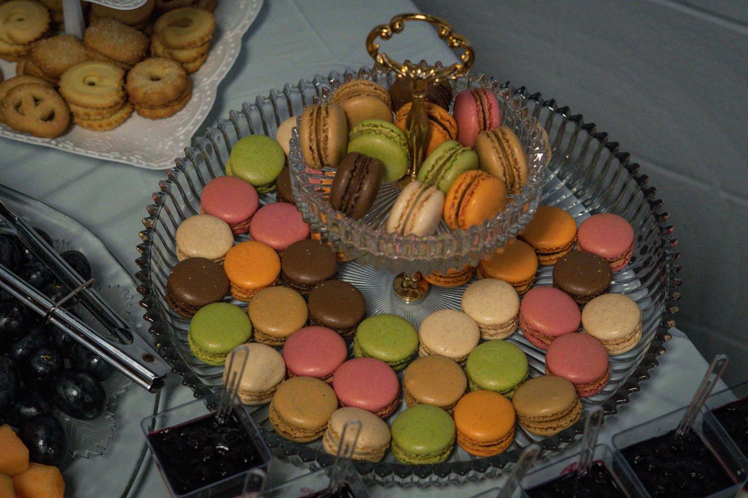 Colorful macarons and cookies arranged on crystal serving platters.