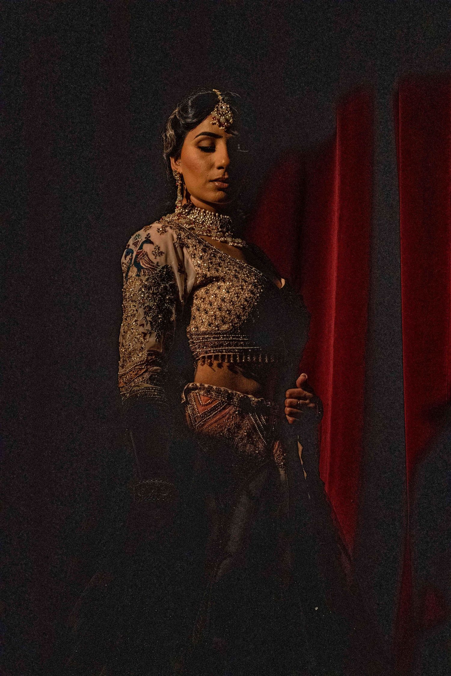 A dramatic portrait in dark lighting showcasing ornate South Asian bridal fashion with intricate gold embellishments and jewelry.