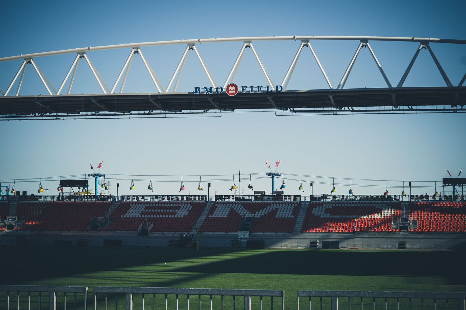 Steel truss bridge structure over stadium seating with red seats visible below.