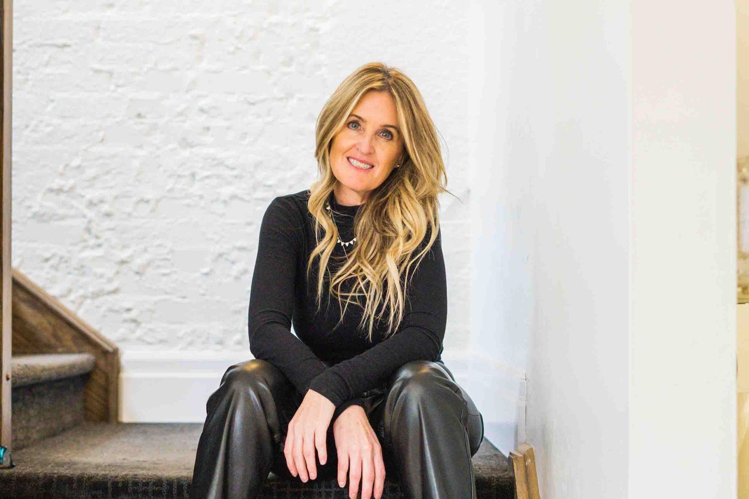 Person in black sweater posing against white textured wall.