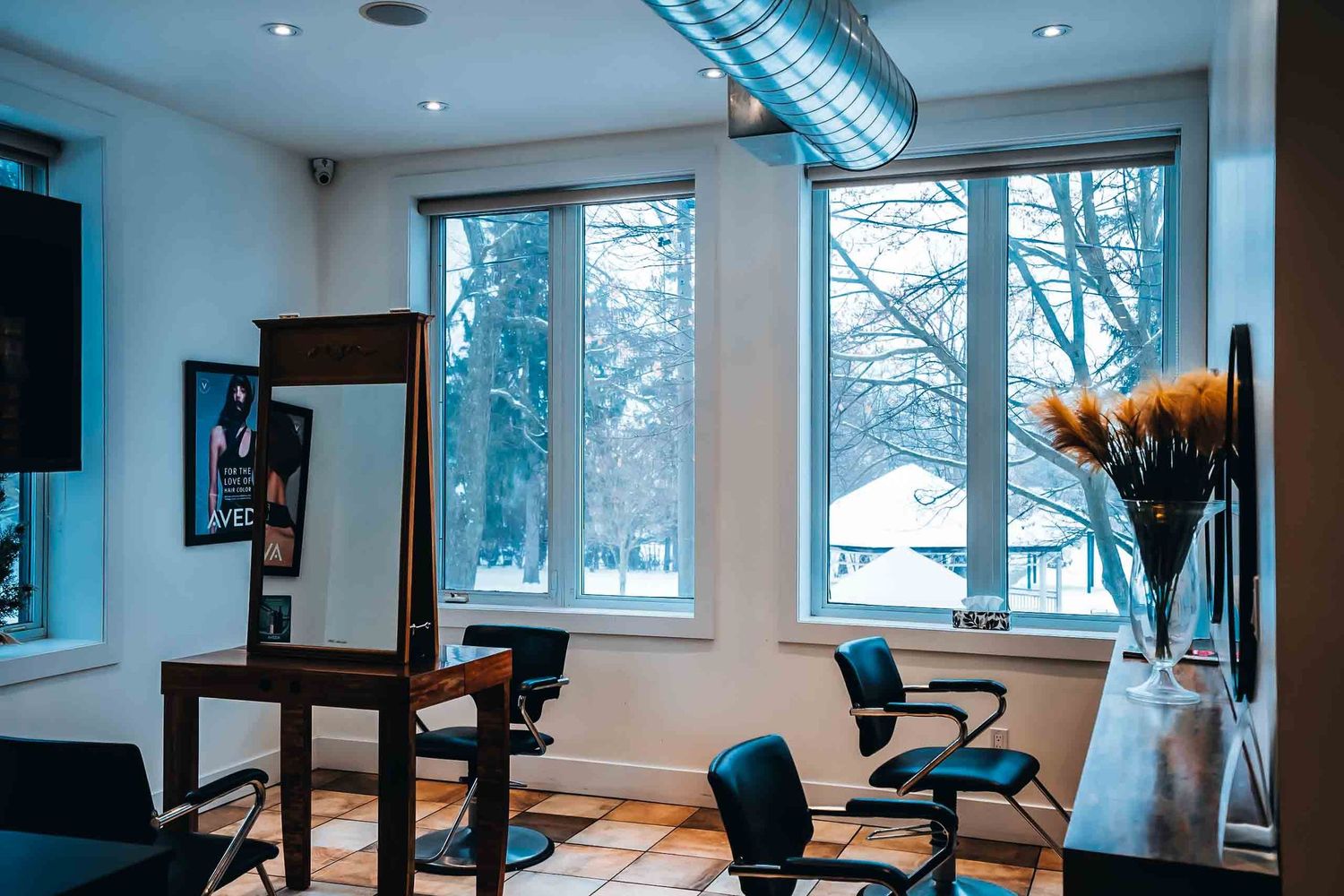 Modern hair salon interior with black styling chairs, mirrors, and snowy winter view through large windows.